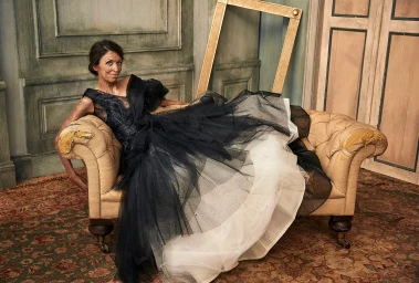 Woman in a black and white tulle ballgown reclining on a tan tufted settee in a classic interior.