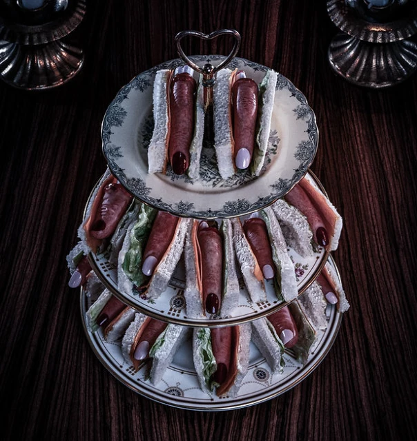 Novelty tier stand displays finger-shaped food on decorative plates. The dark background is dimly lit, creating a moody atmosphere.