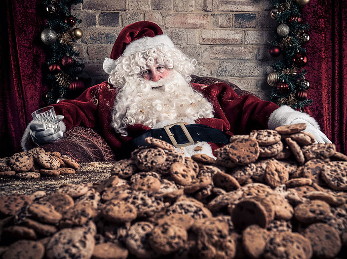 Santa Claus relaxes with a glass of milk, surrounded by piles of chocolate chip cookies in a cozy, festive, indoor setting.