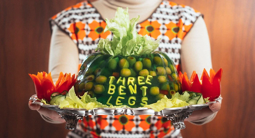 Person holding a tray with green gelatin dessert decorated with olives, lettuce, and carved red bell peppers against wood background.