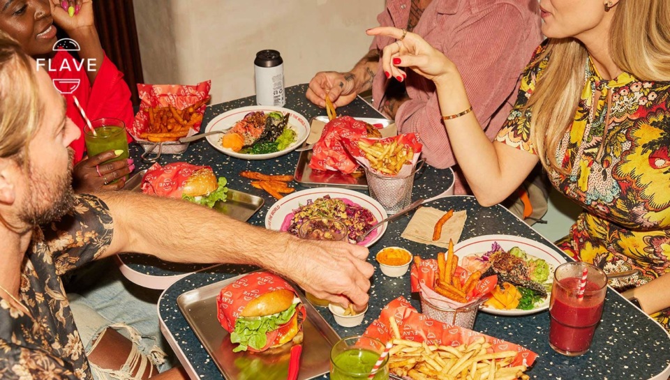 Group of adults at a restaurant table, sharing burgers, fries, and drinks; focus on food, convivial atmosphere, and colorful presentation.