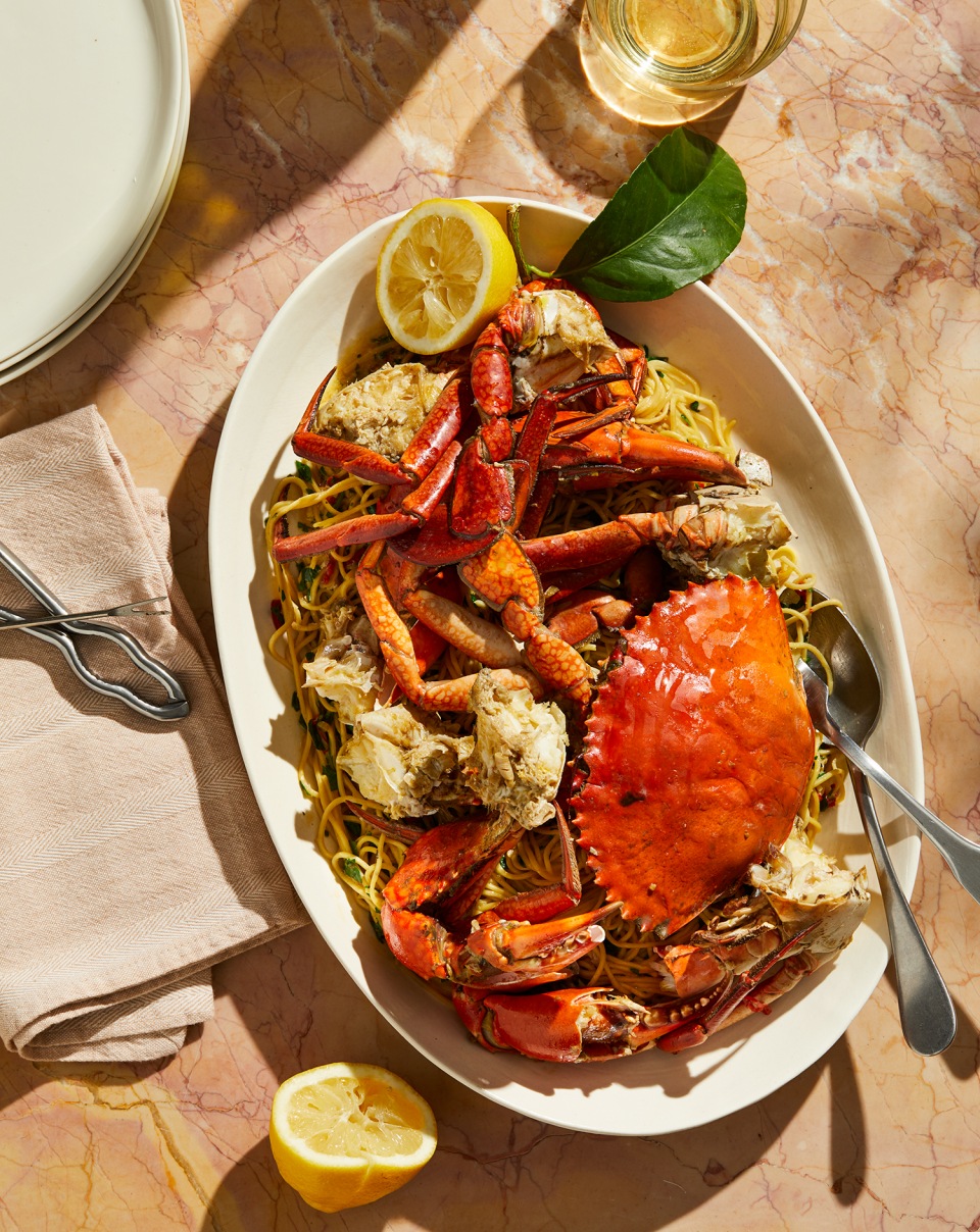 Overhead shot of crab and noodle dish garnished with lemon, served on an oval platter on a marble surface with a linen napkin.