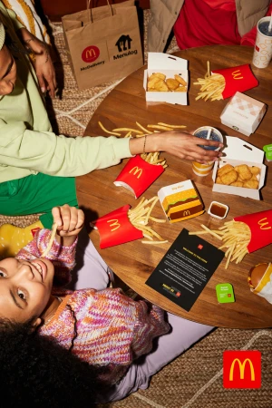 Overhead shot of a child eating McDonald's French fries from a round table with food, drinks, and two other people visible.