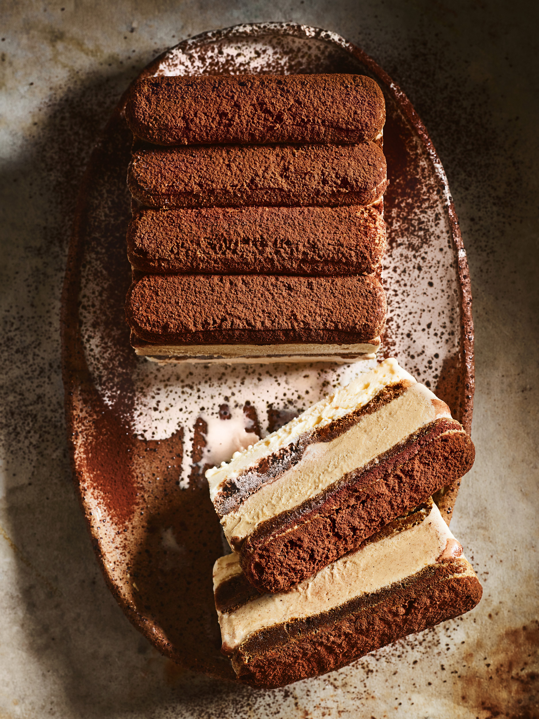 Overhead shot of tiramisu cake with ladyfingers and cocoa powder on a plate, showcasing layers of coffee-flavored dessert.
