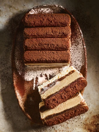 Overhead shot of tiramisu cake with ladyfingers and cocoa powder on a plate, showcasing layers of coffee-flavored dessert.