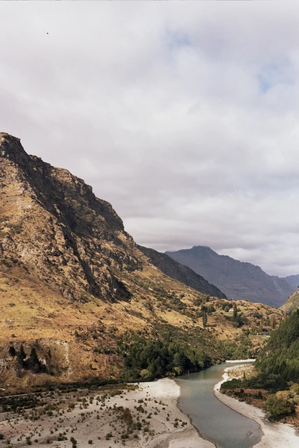 Scenic landscape featuring a winding river cutting through a valley with mountains on either side, under a cloudy sky.