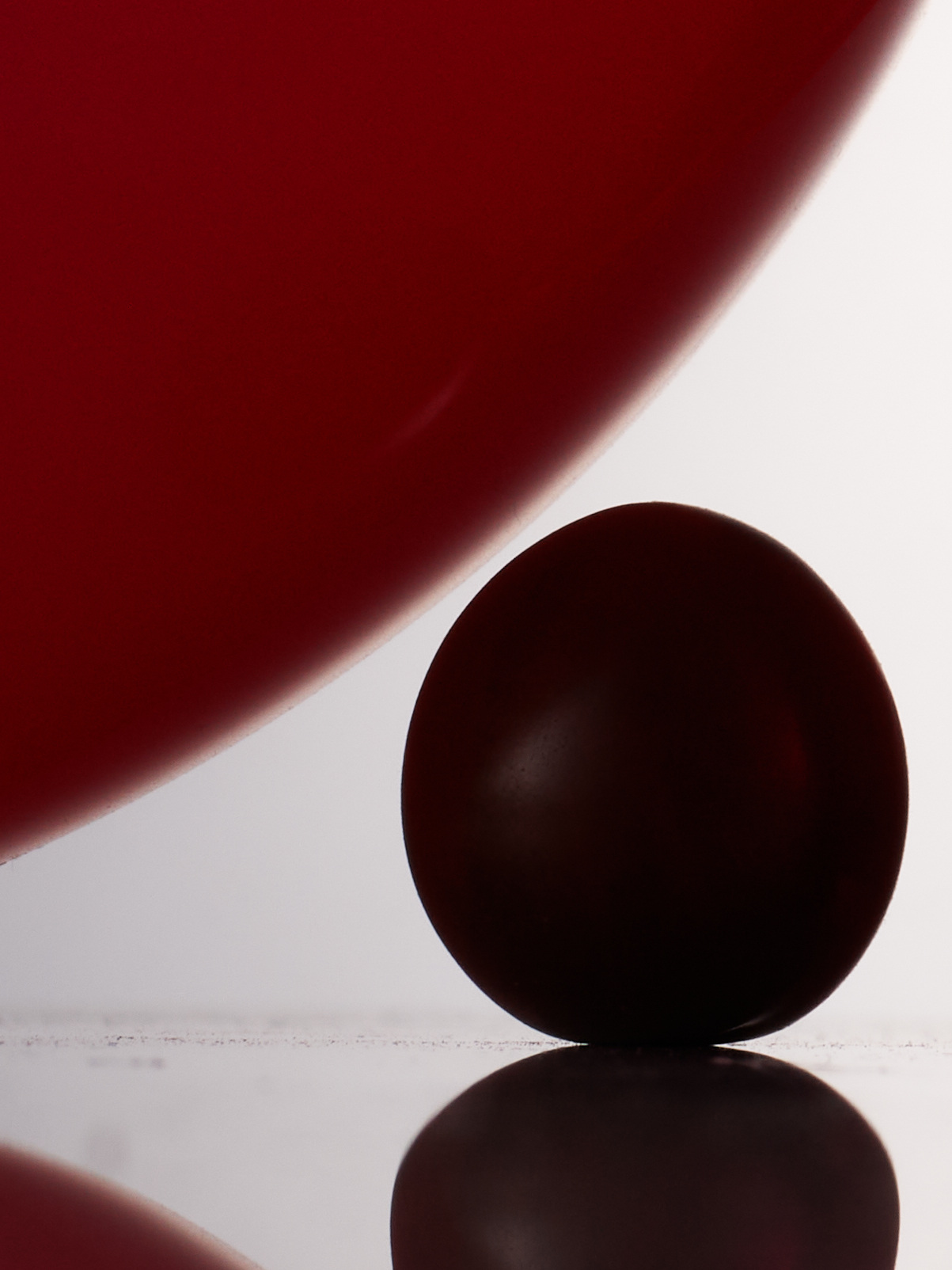 Studio shot of a dark red ball resting on a reflective surface, with a blurred, larger red shape in the background, creating depth.