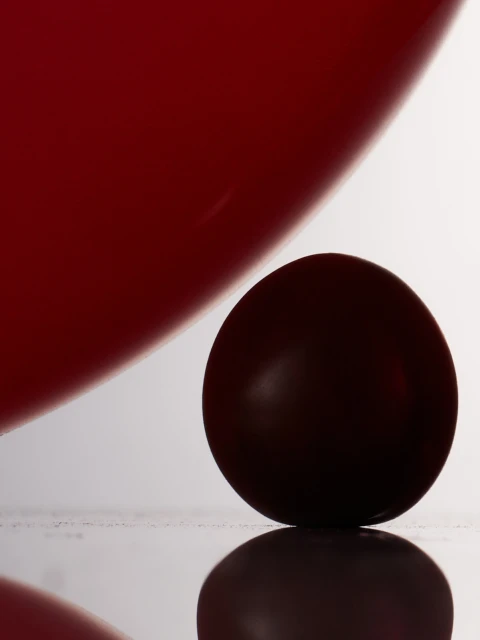Studio shot of a dark red ball resting on a reflective surface, with a blurred, larger red shape in the background, creating depth.