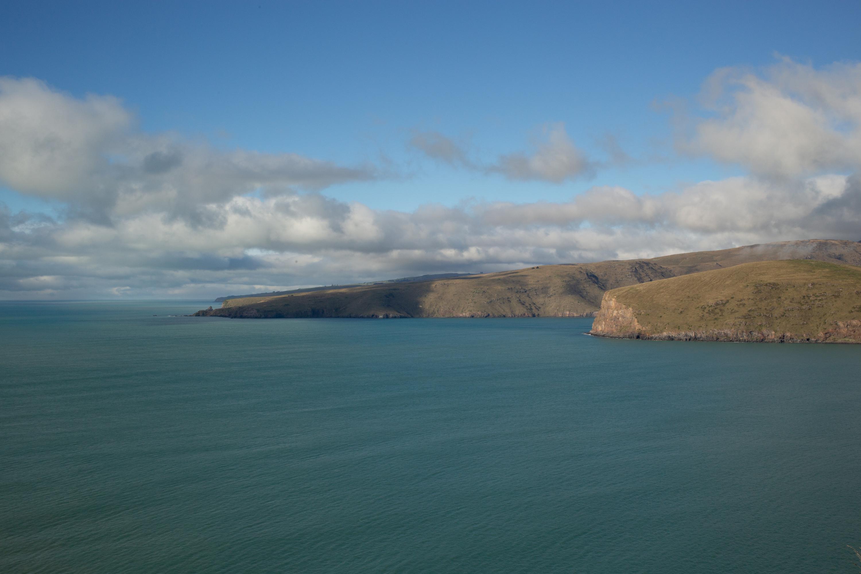 Scenic view of the ocean meeting the coastline, under a blue sky dotted with white clouds on a bright, sunny day.