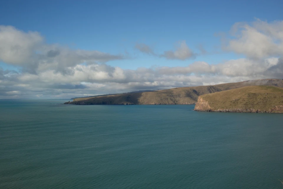 Scenic view of the ocean meeting the coastline, under a blue sky dotted with white clouds on a bright, sunny day. 