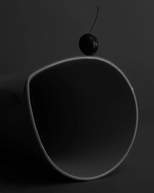 Monochromatic still life: a single cherry resting on the edge of a curved, glossy black surface, emphasizing simplicity and minimalism.