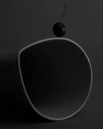 Monochromatic still life: a single cherry resting on the edge of a curved, glossy black surface, emphasizing simplicity and minimalism.