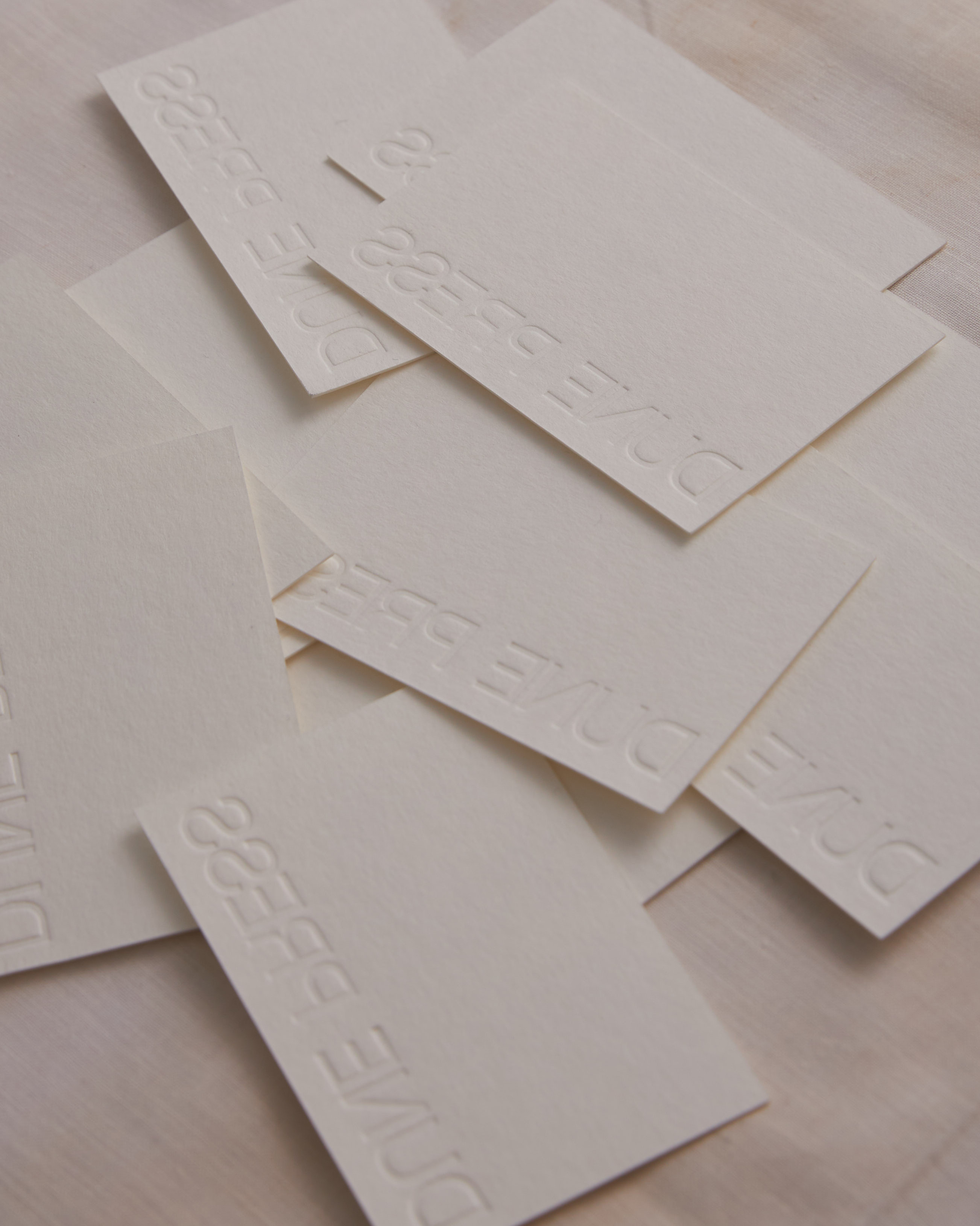 Stack of business cards with embossed text, arranged in a pile on a textured surface, creating a minimalist and tactile effect.