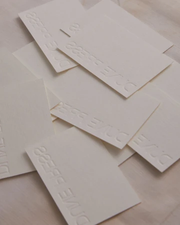 Stack of business cards with embossed text, arranged in a pile on a textured surface, creating a minimalist and tactile effect.
