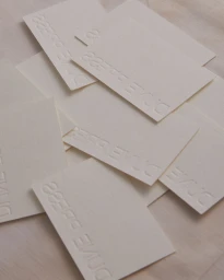 A flat lay composition of scattered white embossed paper cards featuring debossed typography across a textured wooden surface.