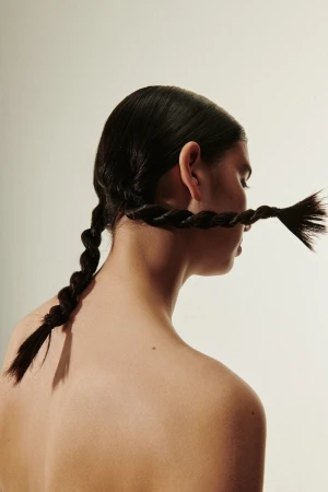 Model with dark hair styled into unique braided ponytails wrapped around the head against a neutral background.