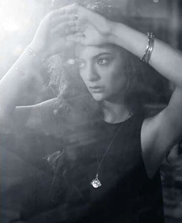 Monochrome portrait of a woman with her hands raised to her forehead wearing bracelets and a pendant necklace