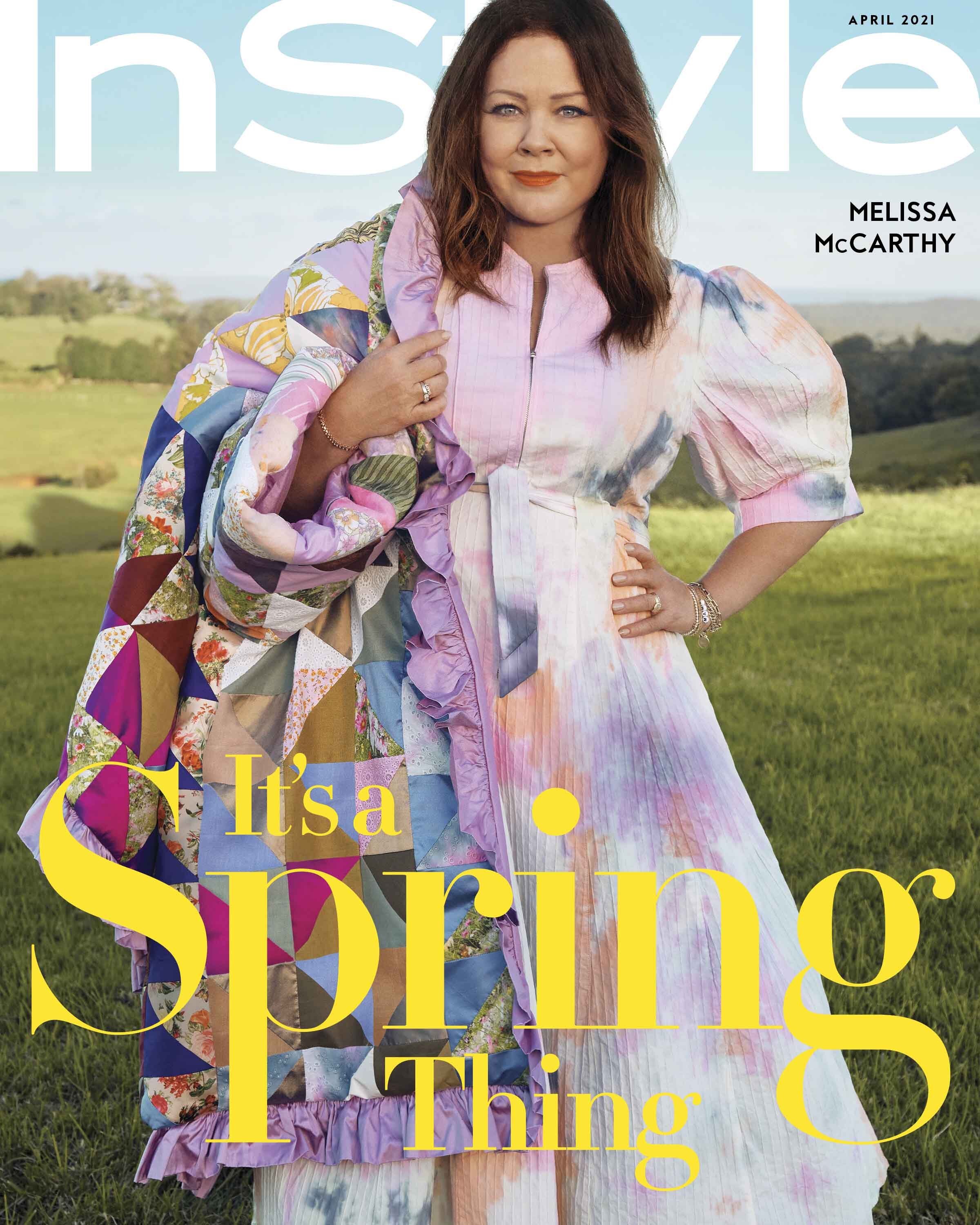 Melissa McCarthy graces a magazine cover wearing a tie-dye dress and a quilt, photographed outdoors in a field with blue sky.