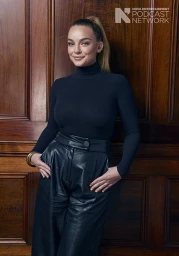Woman with high ponytail wearing black turtleneck and leather trousers against wood wall