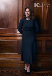 Smiling woman in a dark dress standing against a rich wooden paneled wall