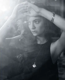 Monochrome portrait of a woman with her hands raised to her forehead wearing bracelets and a pendant necklace