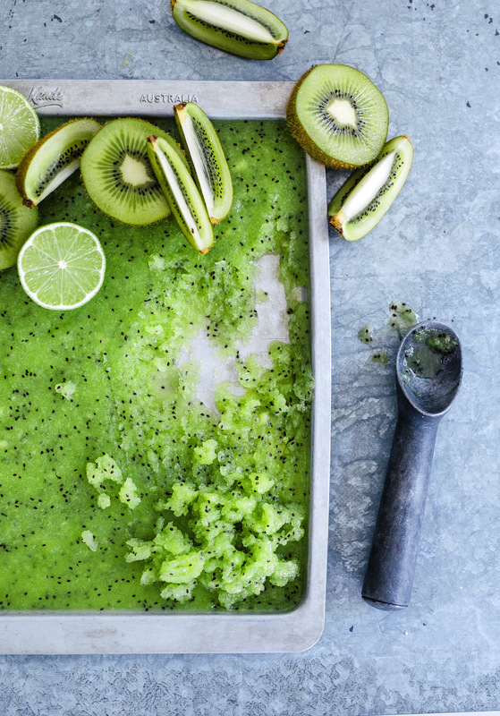 Overhead shot of kiwi lime sorbet in metal pan, garnished with fresh kiwi and lime slices, with a metal ice cream scoop.