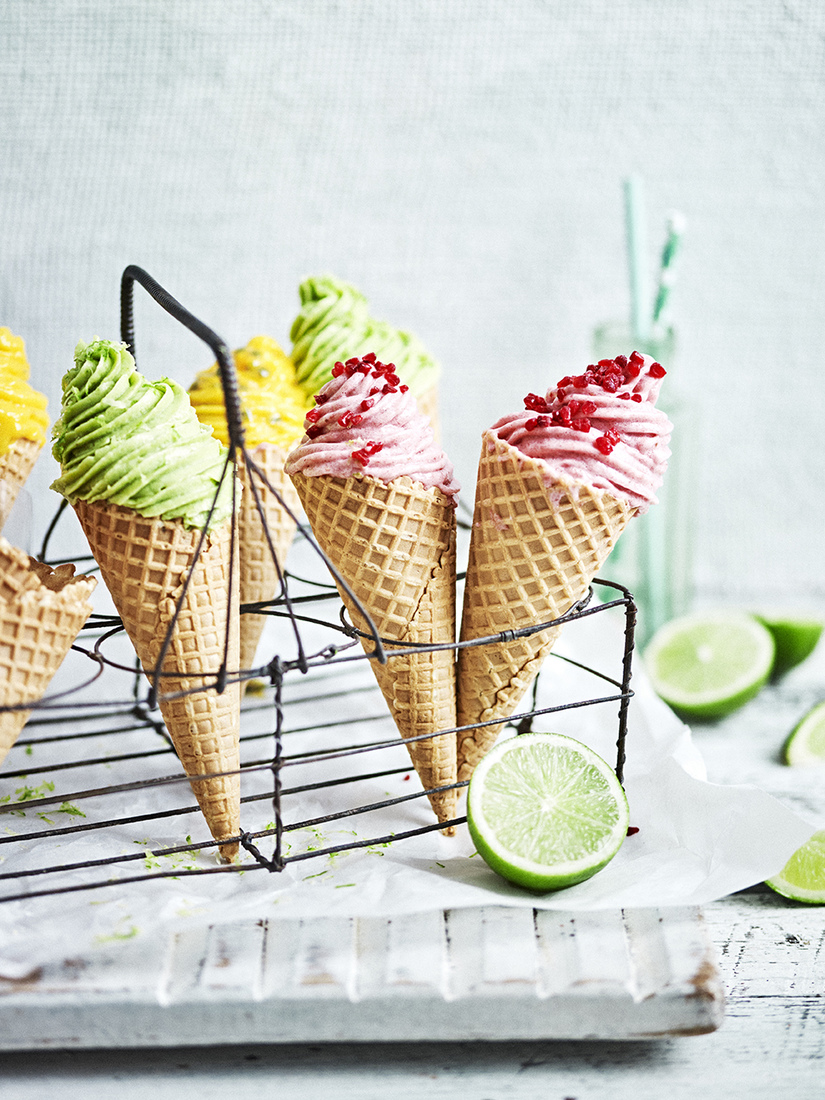 Colorful ice cream cones with various flavors, topped with small red sprinkles, arranged in a black wire rack, food photography.