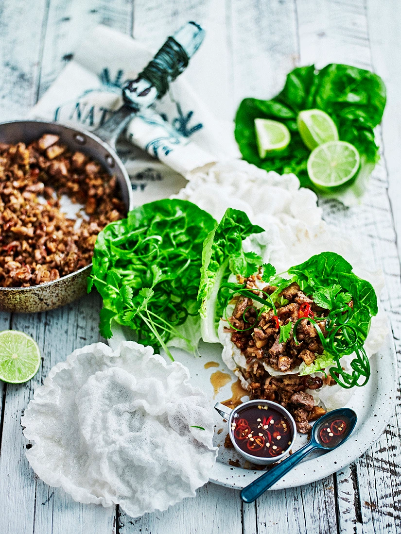 Lettuce cups filled with savory mince, fresh herbs, lime wedges, and a small bowl of chili dipping sauce styled by Olivia Blackmore