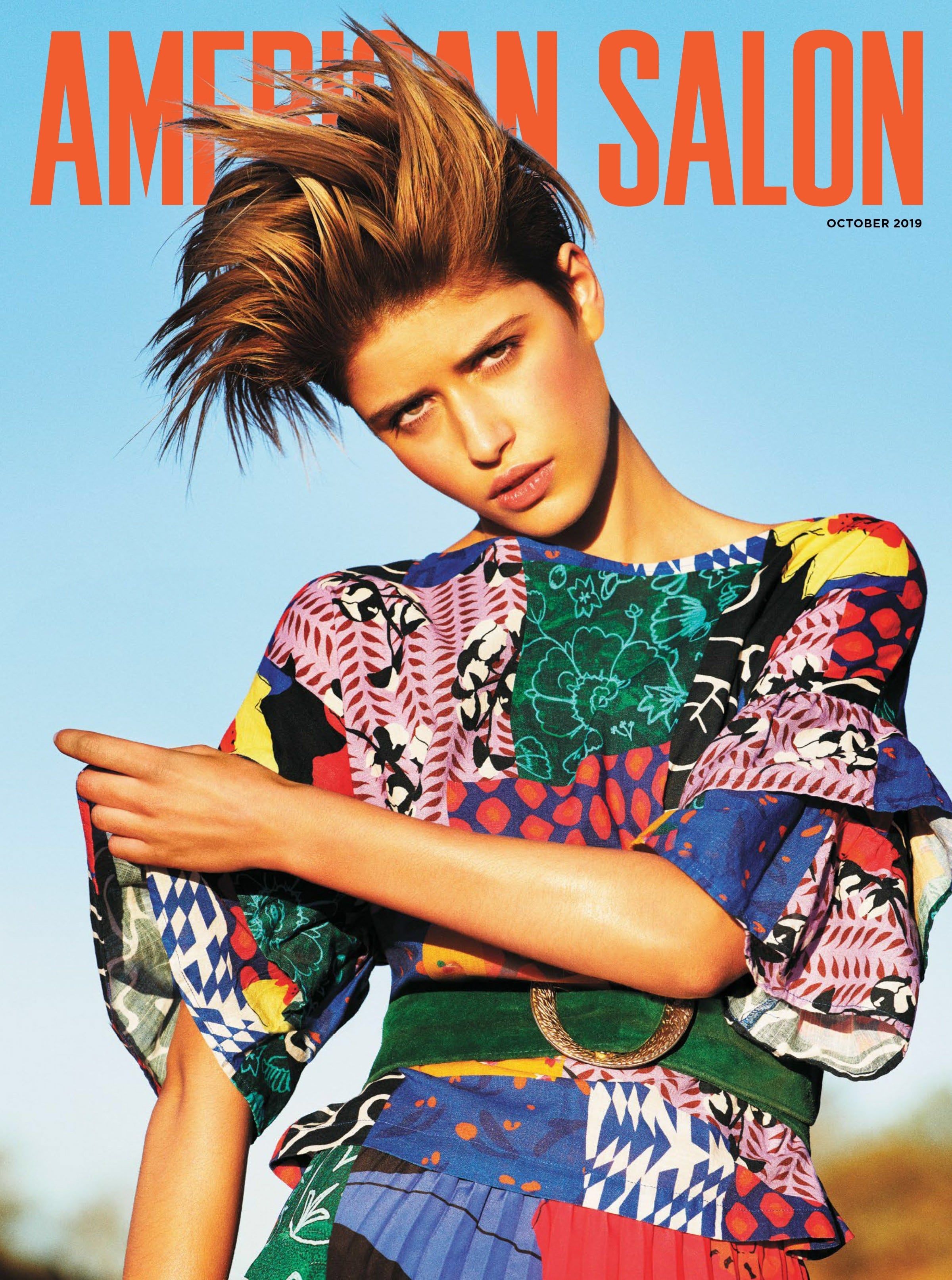 Magazine cover featuring a young woman with spiky blonde hair, wearing a colorful patchwork dress against a light blue sky backdrop.