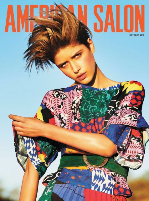 Magazine cover featuring a young woman with spiky blonde hair, wearing a colorful patchwork dress against a light blue sky backdrop.