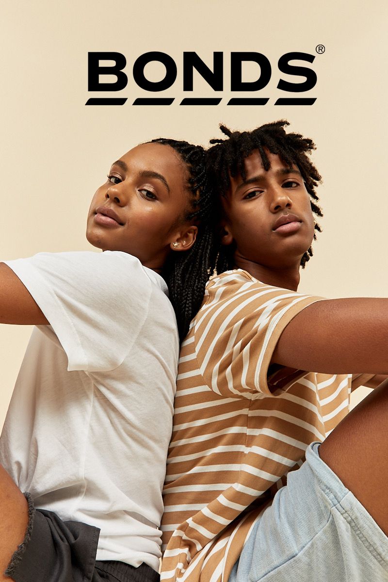 Two young adults pose back-to-back, wearing casual t-shirts and shorts, against a neutral background with the Bonds logo overhead.