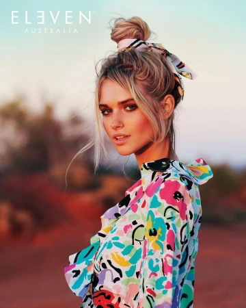 Portrait of a blonde woman wearing a colourful floral top and a patterned hair scarf tied in a bun in an outdoor landscape setting