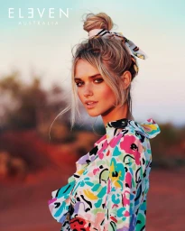 Portrait of a blonde woman wearing a colourful floral top and a patterned hair scarf tied in a bun in an outdoor landscape setting
