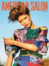Model with spiky brown hair wearing a colourful patterned top and green belt against a clear blue sky.