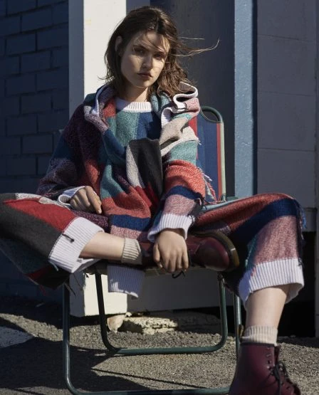 Fashion portrait of a young adult female model sitting outdoors, wearing a multi-colored knit outfit and reddish brown boots.