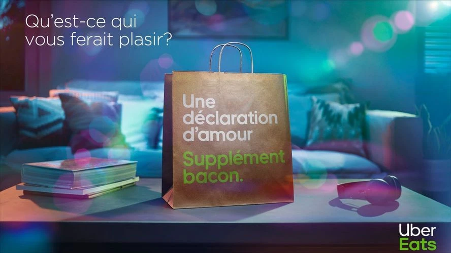 Studio shot of a paper shopping bag with the text 'Une déclaration d'amour Supplément bacon.' and the Uber Eats logo.