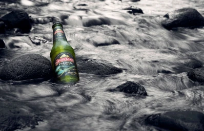 Green beer bottle standing among wet dark rocks in a flowing stream with silky water motion