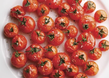 Close-up overhead shot of blistered cherry tomatoes on the vine, sprinkled with coarse sea salt and cracked black pepper.