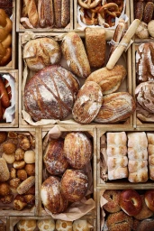 Top-down view of various artisan breads and baked goods arranged in wooden crates lined with paper.