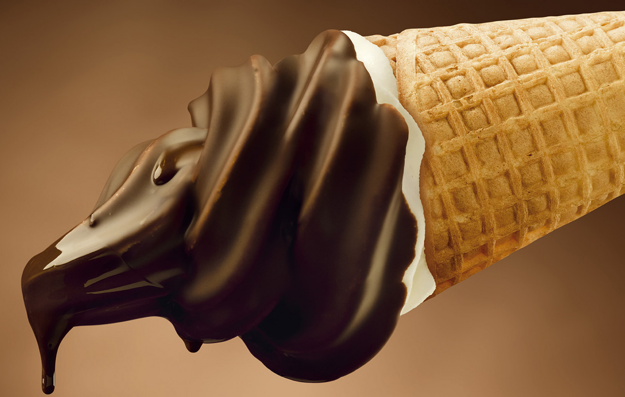Close-up of a chocolate ice cream cone with melting chocolate against a brown background, perfect for dessert and food photography.