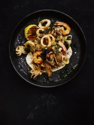 Overhead food photography of fried seafood platter with shrimp, squid rings, and grilled lemon on dark plate