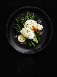 Poached eggs with hollandaise sauce and asparagus spears served on a dark round plate