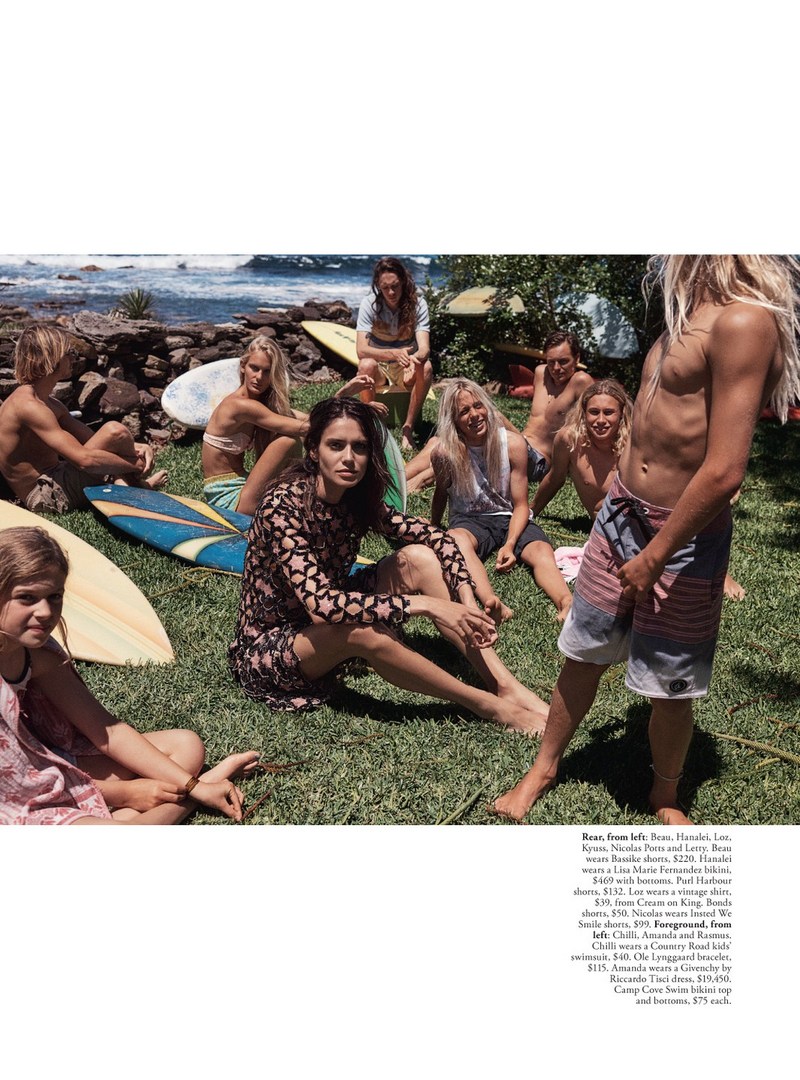Group of young people sit on the grass with surfboards near the ocean, enjoying a sunny day. Fashion and beach lifestyle.