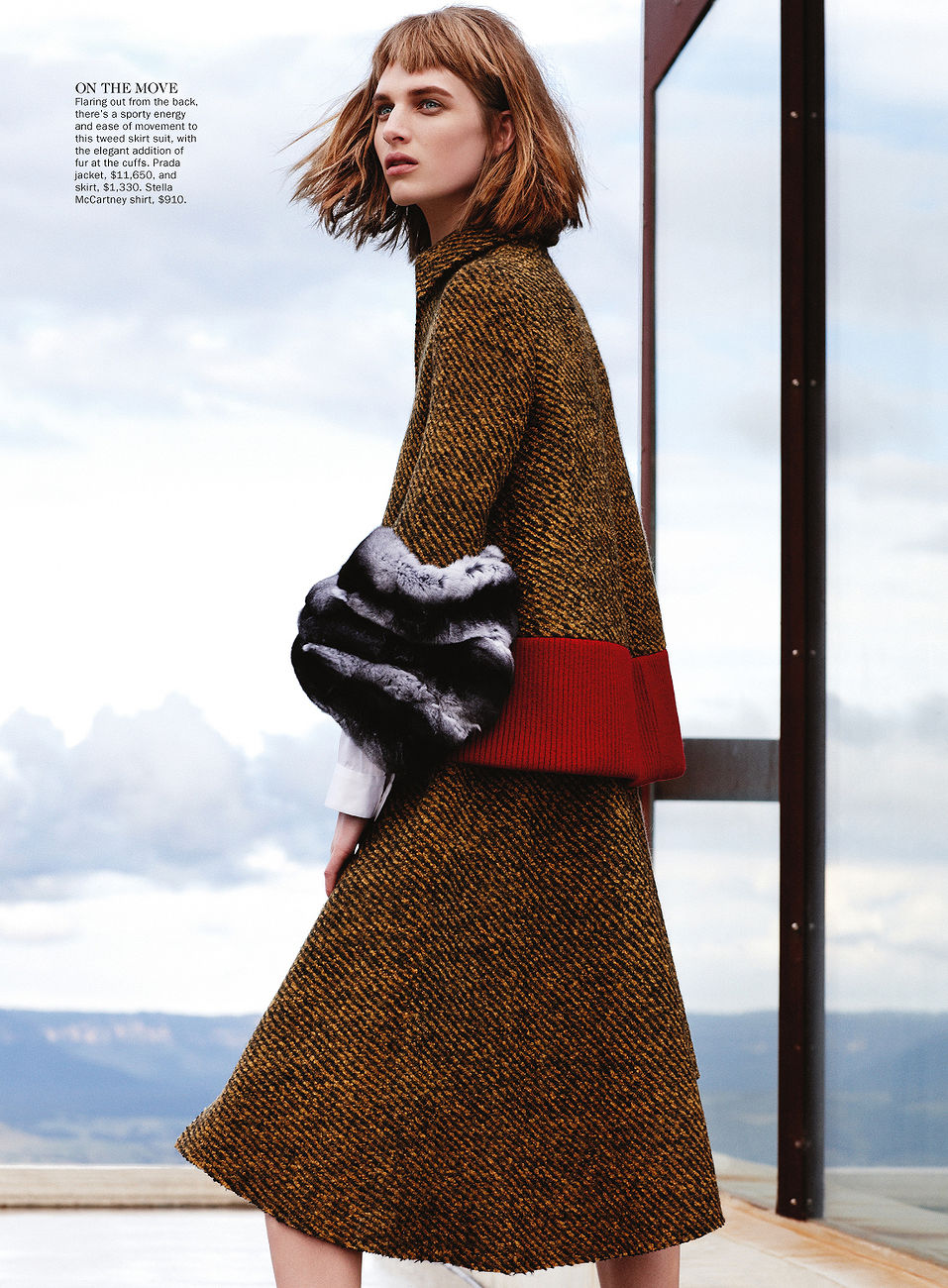 Fashion editorial shot of a model wearing a patterned skirt and jacket, accented with faux fur sleeves, posing in an outdoor setting.