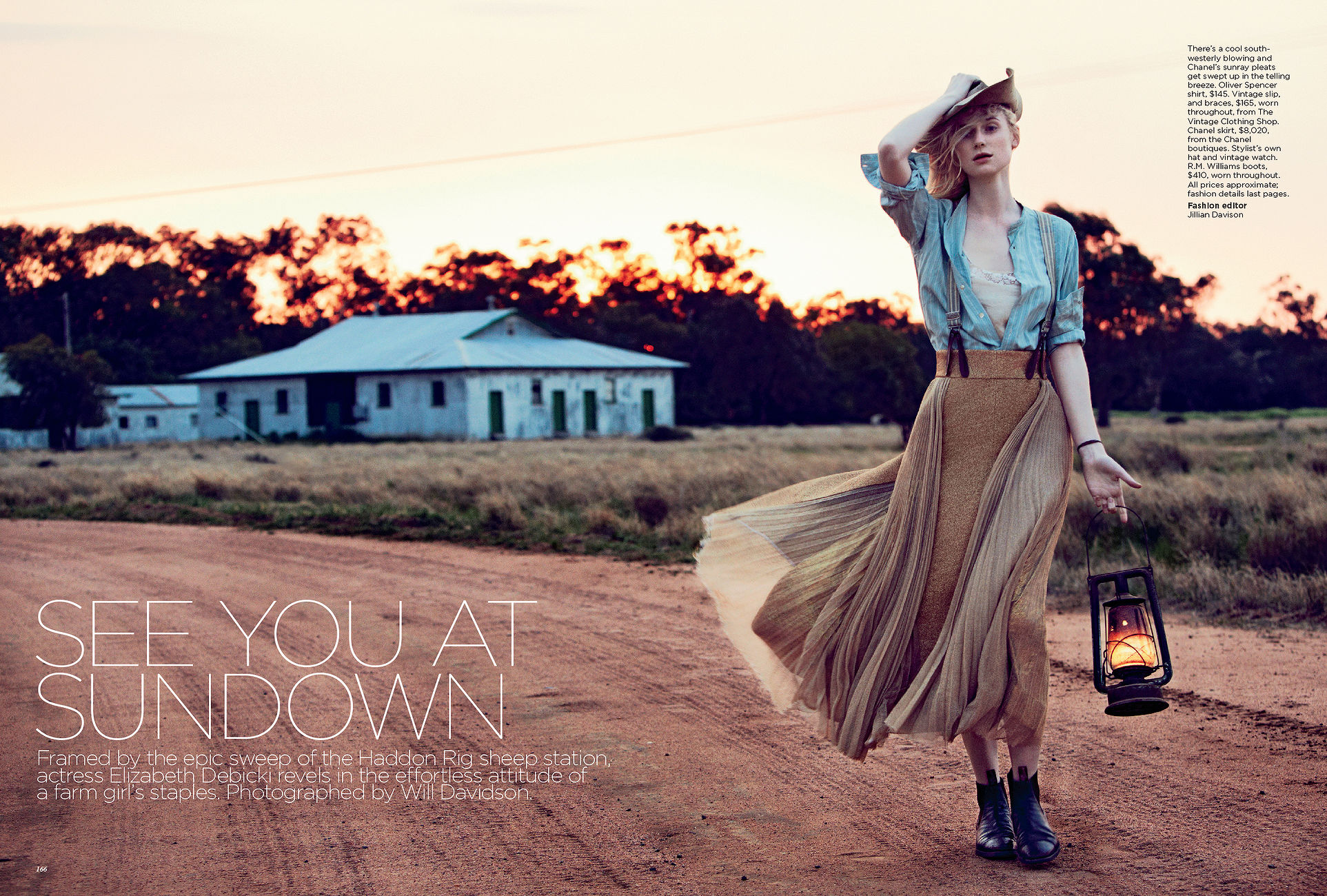 Blonde woman in a prairie dress stands in a field at sunset, holding a lantern and wearing a cowboy hat in a fashion editorial.