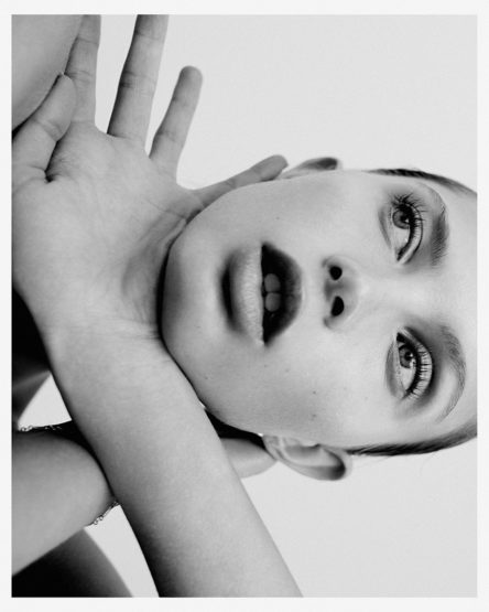 Striking black and white portrait of a woman with crossed arms, emphasizing her eyes and lips in a close-up composition against a white backdrop.