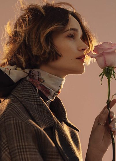 Portrait of a woman in a patterned coat holding a rose, with soft lighting, neutral background, and shallow depth of field.
