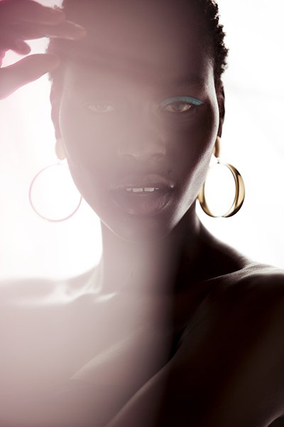 Close-up studio portrait of an adult female with gold hoop earrings and blue eyeshadow, accented by soft, diffused lighting.