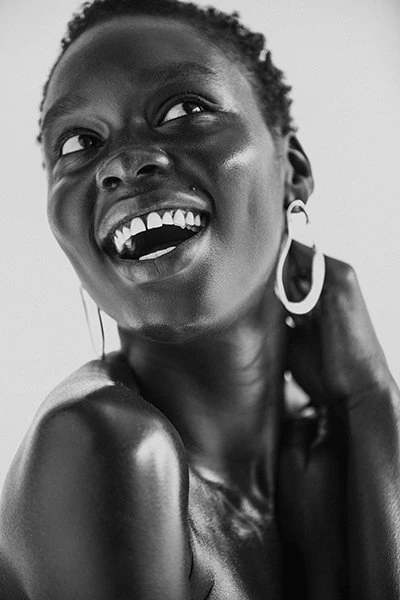Black and white portrait of a Black woman smiling and looking up, wearing hoop earrings. The image is well-lit.