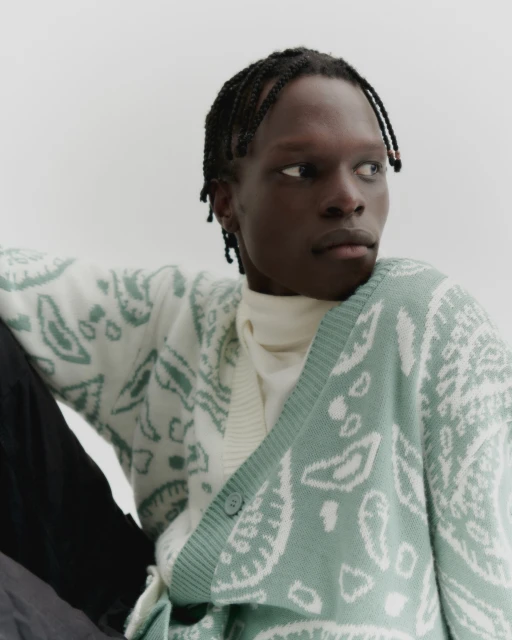 Portrait of an adult Black male in a patterned cardigan and turtleneck against a white background in a fashion forward style.